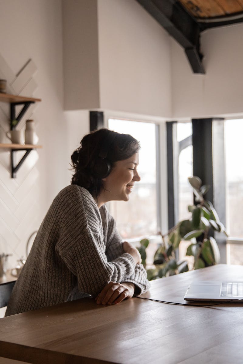 A woman enjoys a video call on her laptop in a modern, cozy kitchen setting with natural light.